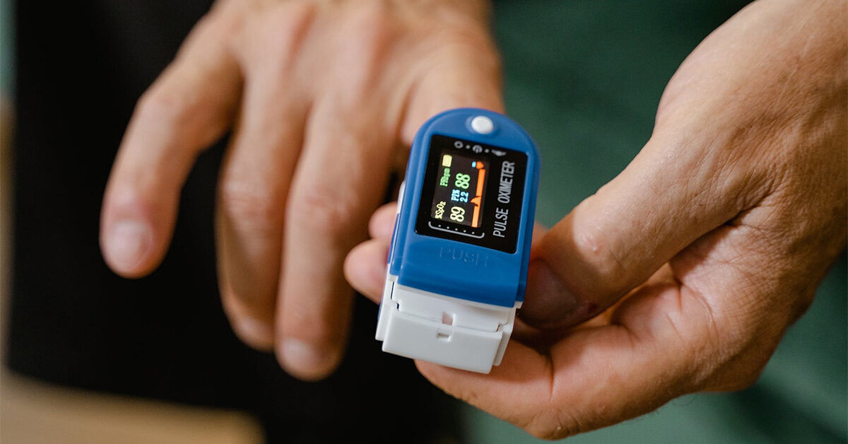 a photograph of a pulse oximeter being used. This device uses pulse oximetry to measure blood oxygen content in the blood, and your pulse rate. what is pulse oximetry